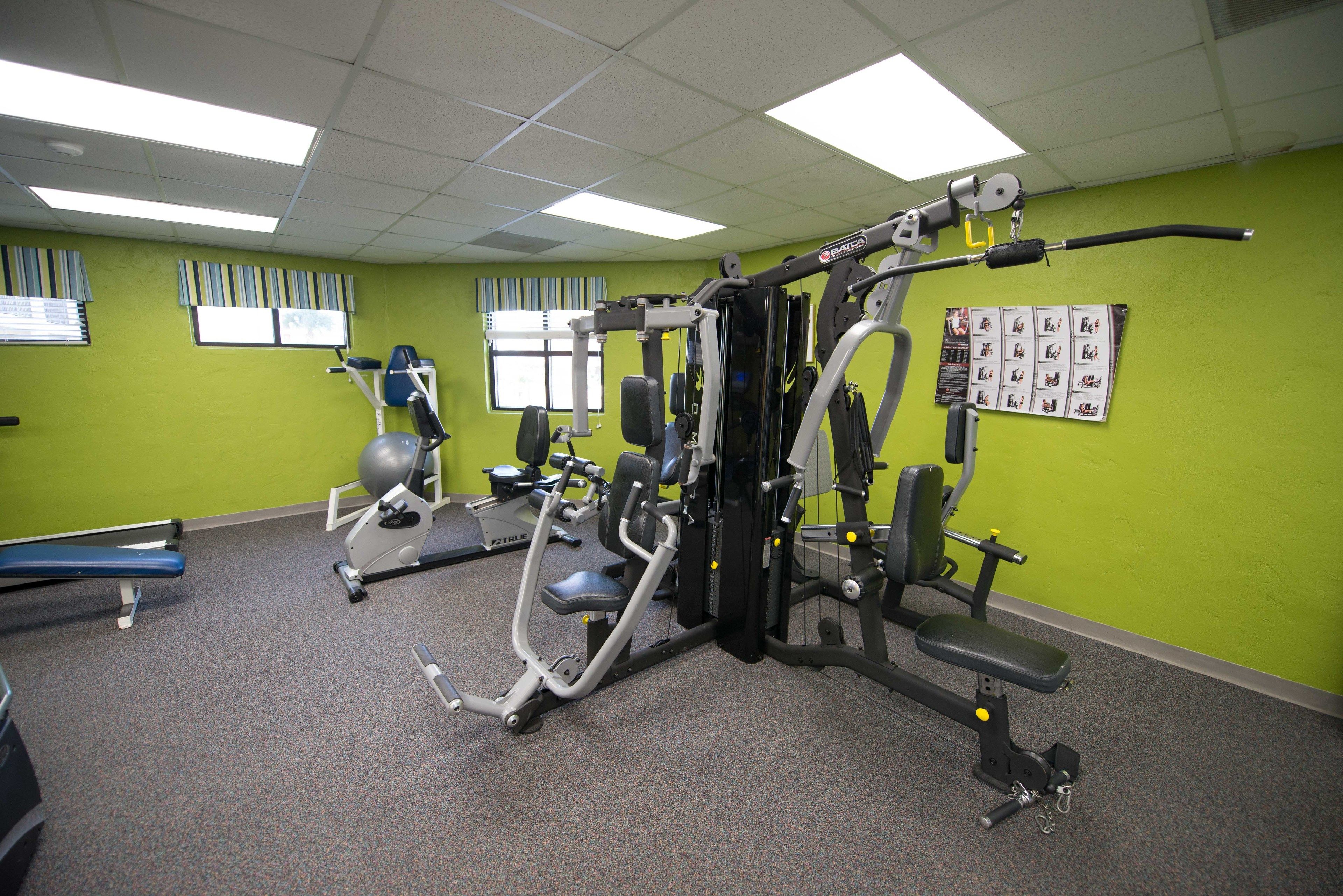 A gym with various exercise equipment, a bench, and a wall with a bulletin board.