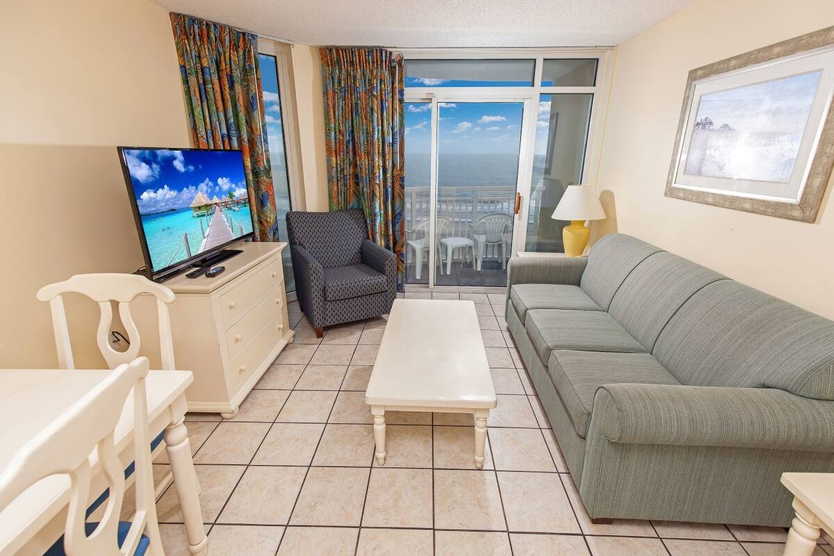 Sala de estar com televisão, sofá, mesa de centro e varanda com vista.