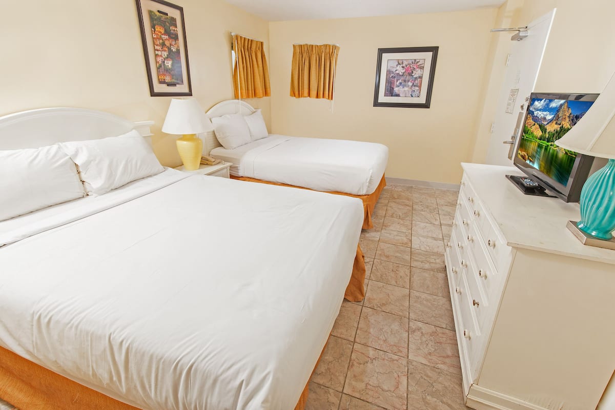 Quarto de hotel com duas camas, televisão, cómoda e abajur.