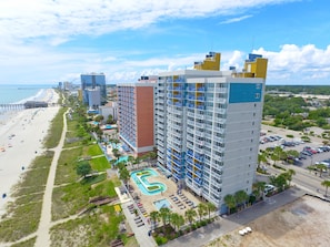 A high-rise hotel with multiple balconies, a swimming pool, and a beach view.
