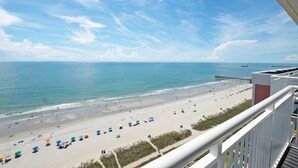 Une vue sur la plage depuis un balcon, avec une jetée visible au loin.