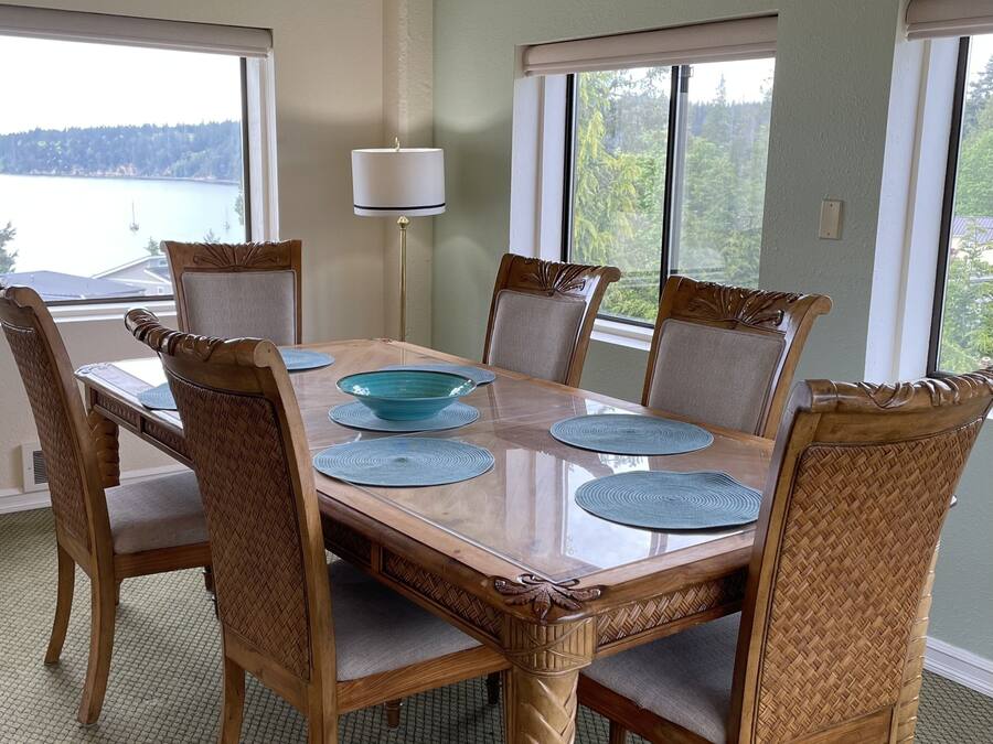 Een eetkamer met een grote tafel, zes stoelen en uitzicht op een meer door grote ramen.