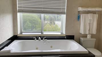 Een badkamer met een groot bad, een toilet en een raam met zonwering.