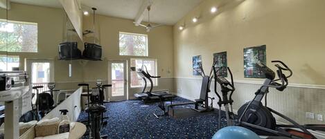Une salle de sport équipée de matériel d’exercice, dotée d’un ventilateur de plafond et de grandes fenêtres.