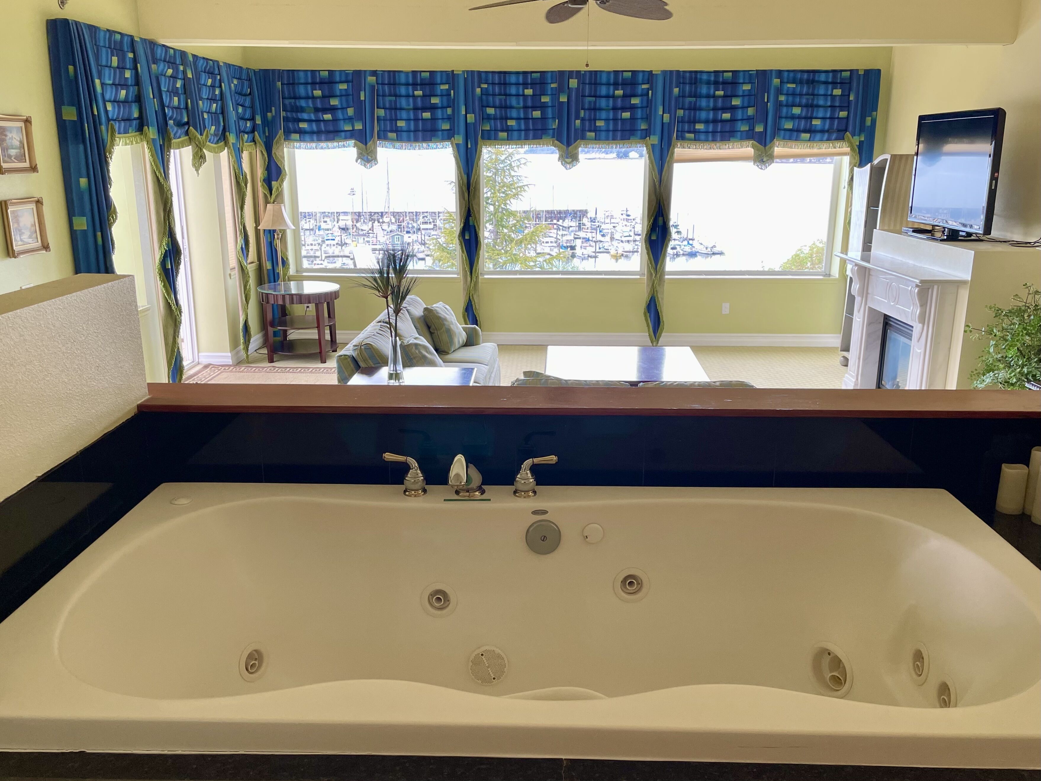Un baño con una bañera grande, un espejo y vistas a un puerto deportivo por la ventana.