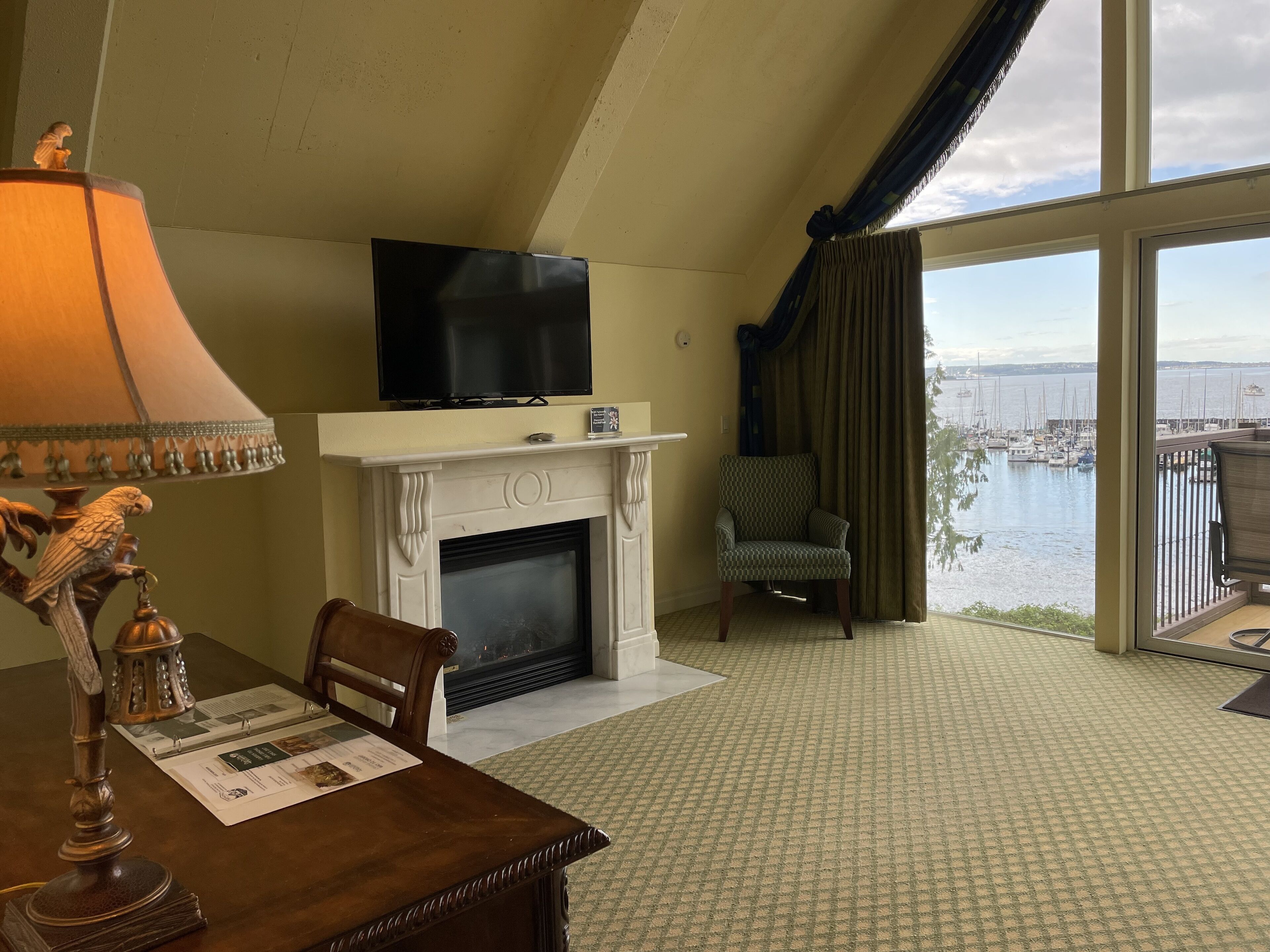 A room with a fireplace, a television, a dining table with chairs, and a view of a marina through large windows.