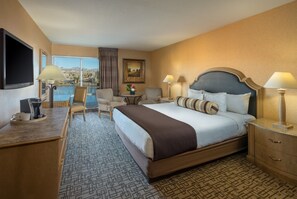 A hotel room with a large bed, a desk with a coffee maker, a chair, a TV, and a view of a body of water.
