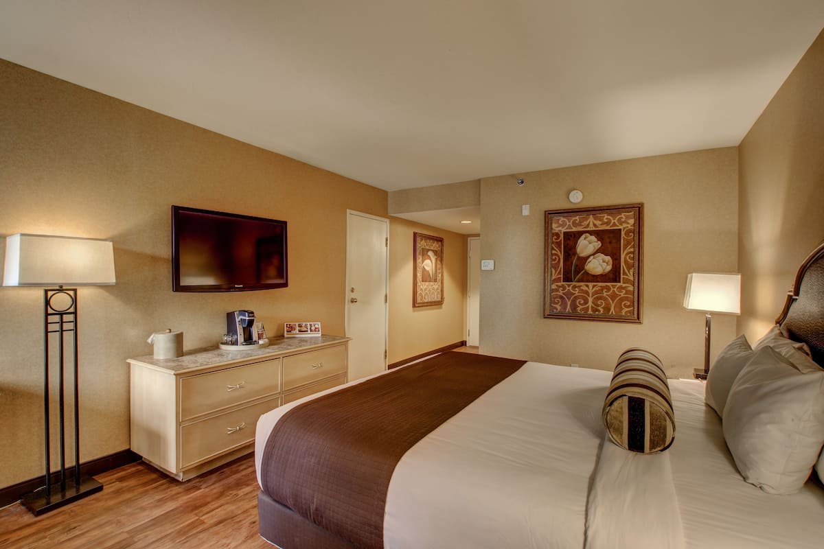 Ein Hotelzimmer mit einem großen Bett, einem Schreibtisch mit Kaffeemaschine, einem Flachbildfernseher und einem gerahmten Bild an der Wand.