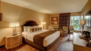 Una habitación de hotel con una cama grande, dos mesitas de noche, un escritorio, una silla y una ventana con cortinas.