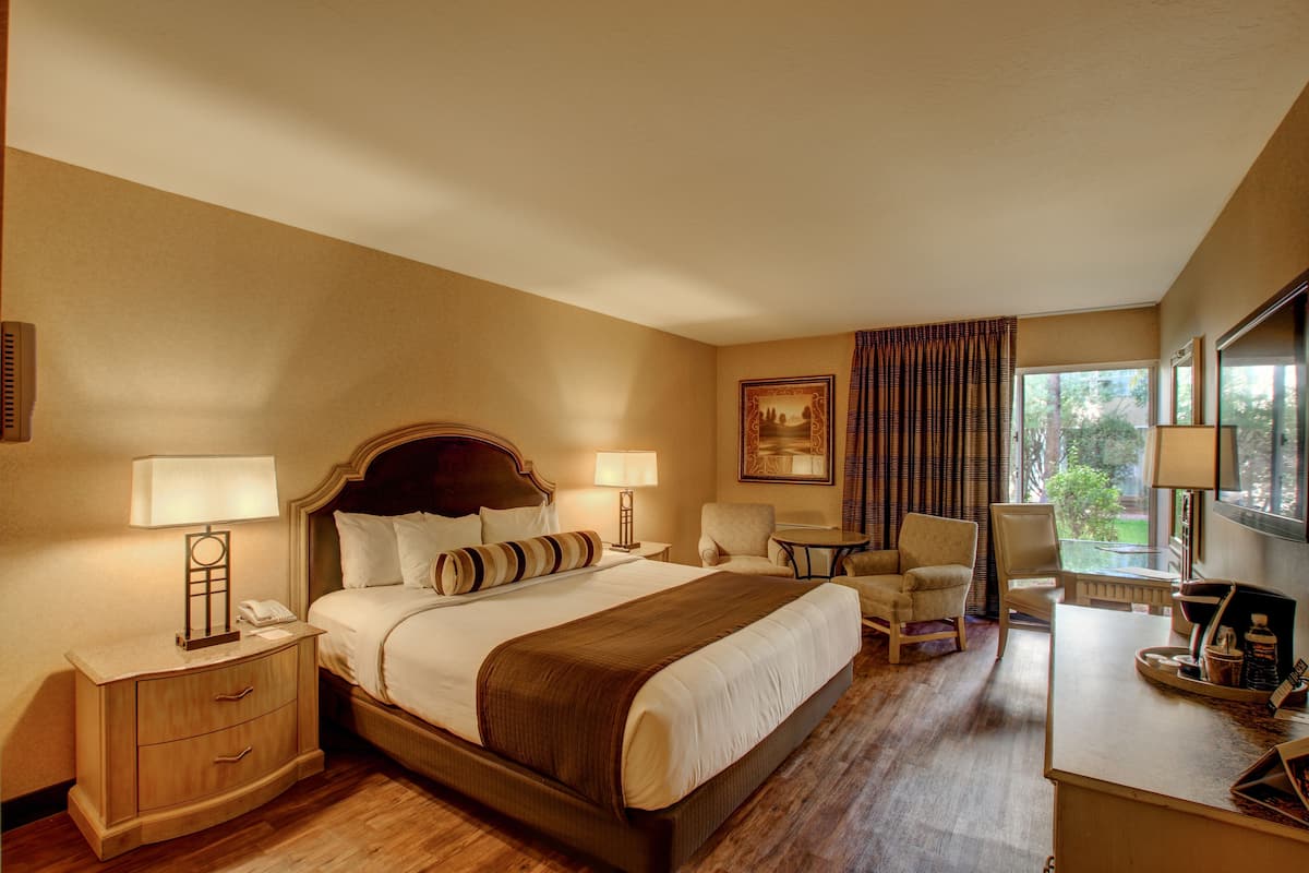 Ein Hotelzimmer mit einem großen Bett, zwei Nachttischen, einem Schreibtisch, einem Sessel und einem Fenster mit Vorhängen.