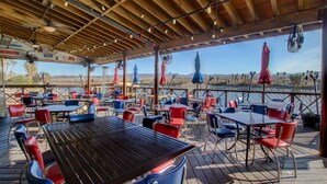 Un patio exterior con mesas y sillas, techo de madera y vistas al paisaje.