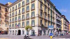 Un edificio de varios pisos con fachada amarilla, múltiples balcones y un cartel que indica direcciones a Milán.