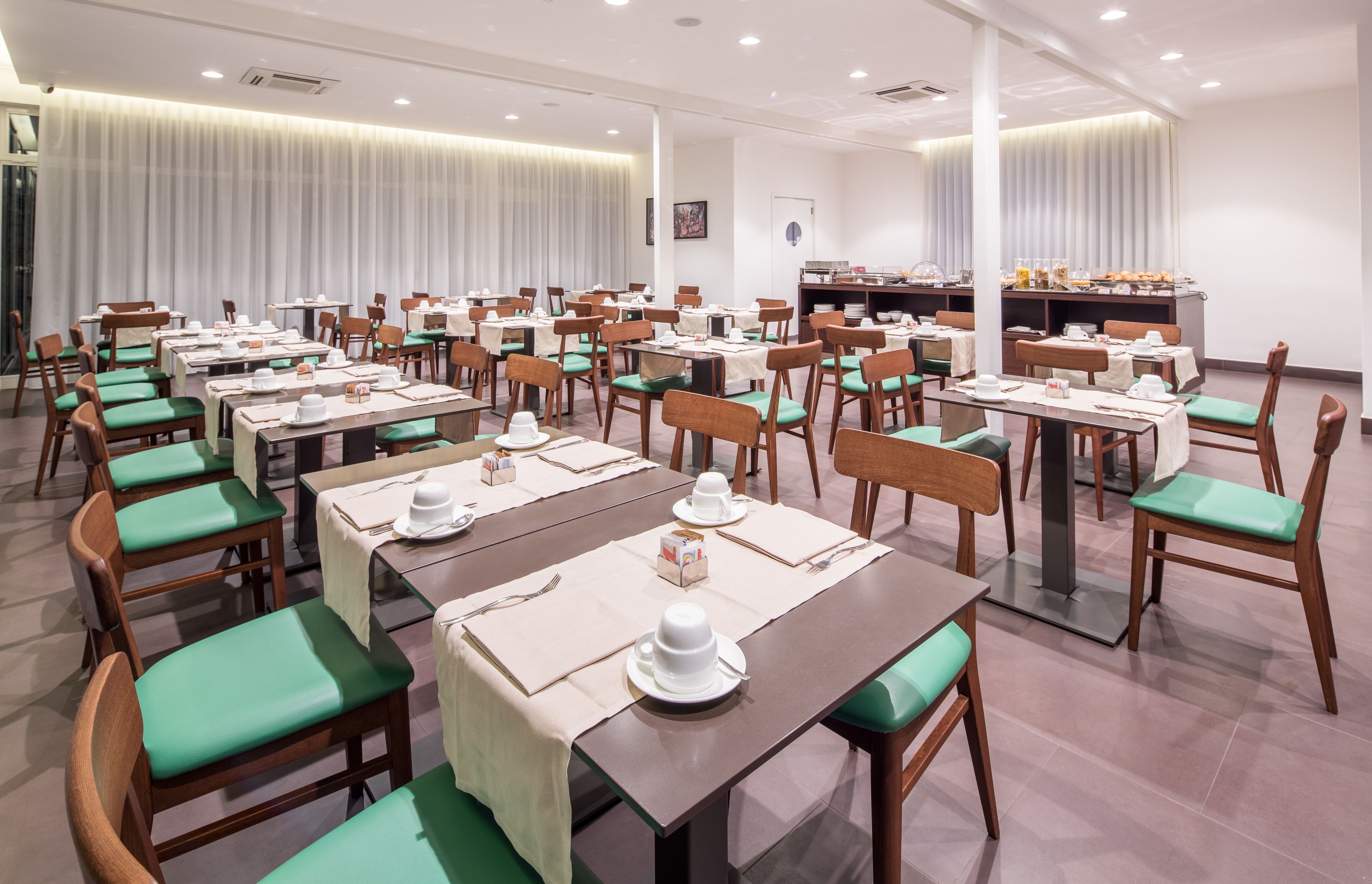 Un comedor con varias mesas y sillas, cada conjunto con vajilla y servilletas.