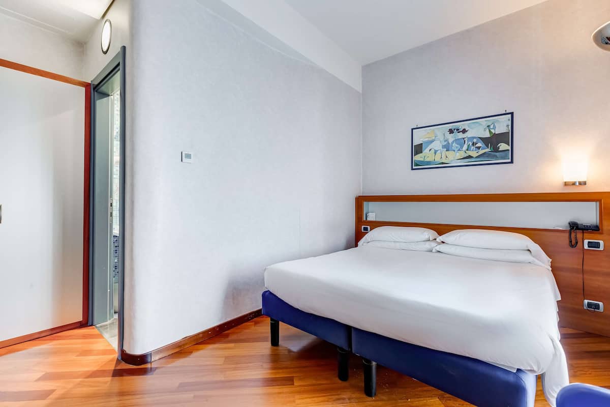Una habitación de hotel con una cama, un cuadro en la pared y suelo de madera.