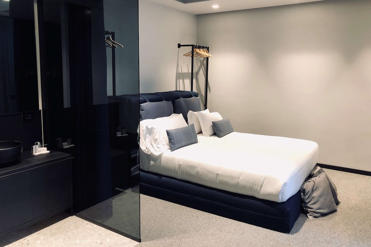 Un dormitorio moderno con una cama grande, una mesita de noche, un espejo y un armario.