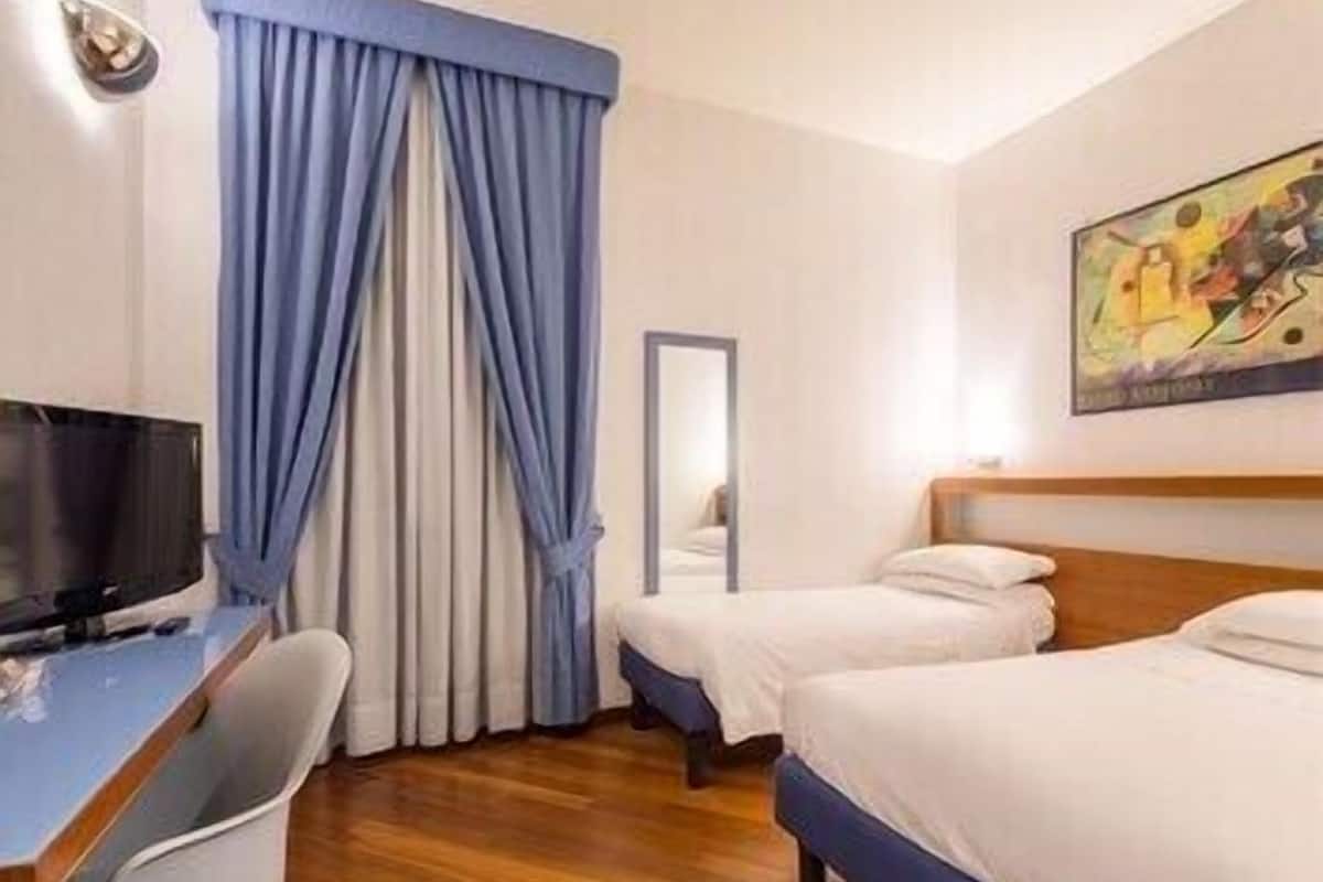 Habitación de hotel con piso de madera, un escritorio con televisor, dos camas y un cuadro en la pared.