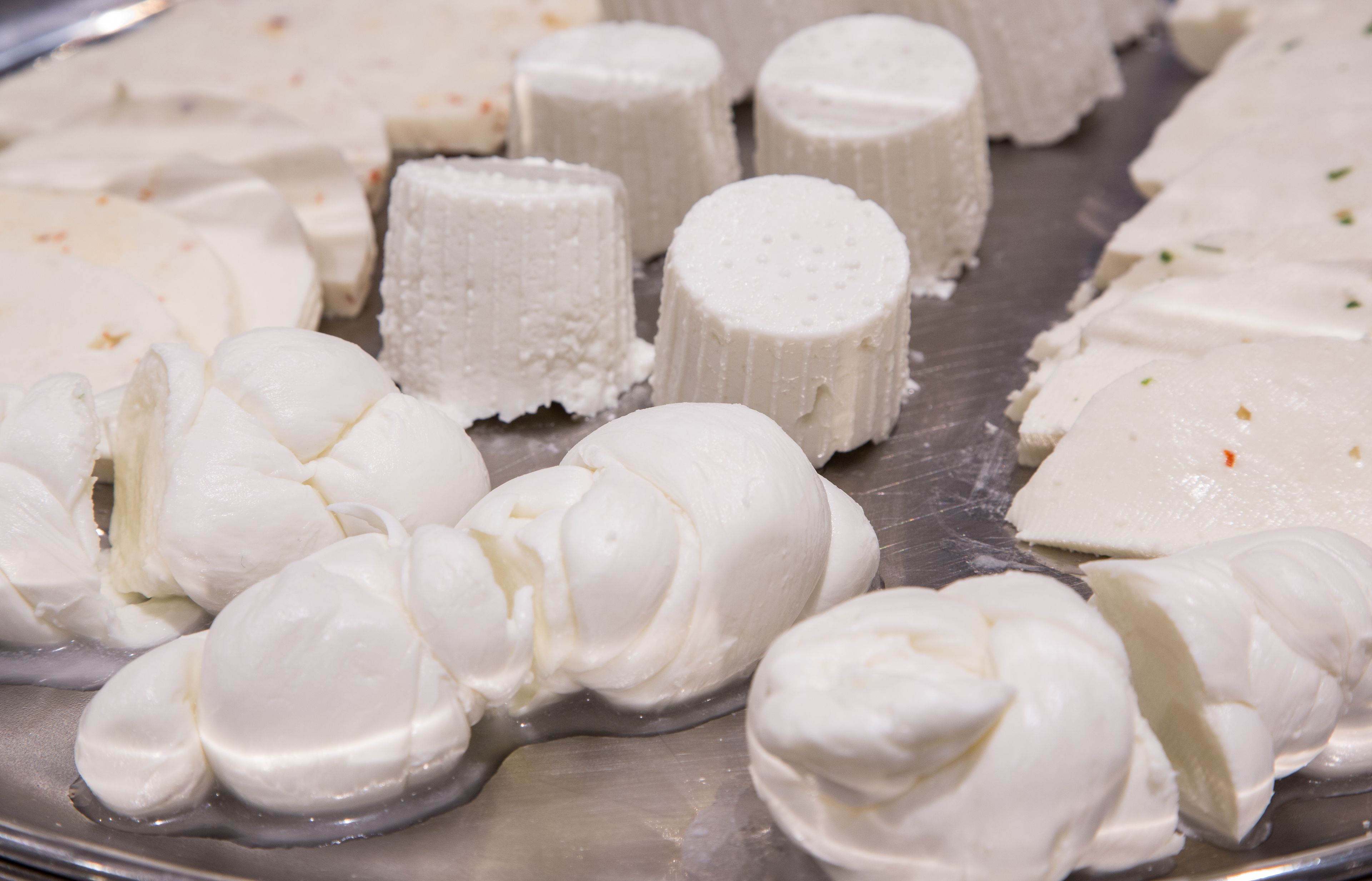 A variety of white, cylindrical and rounded cheese items on a metal tray.