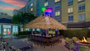 An outdoor bar area with a thatched roof, bar stools, and a tiki bar sign.