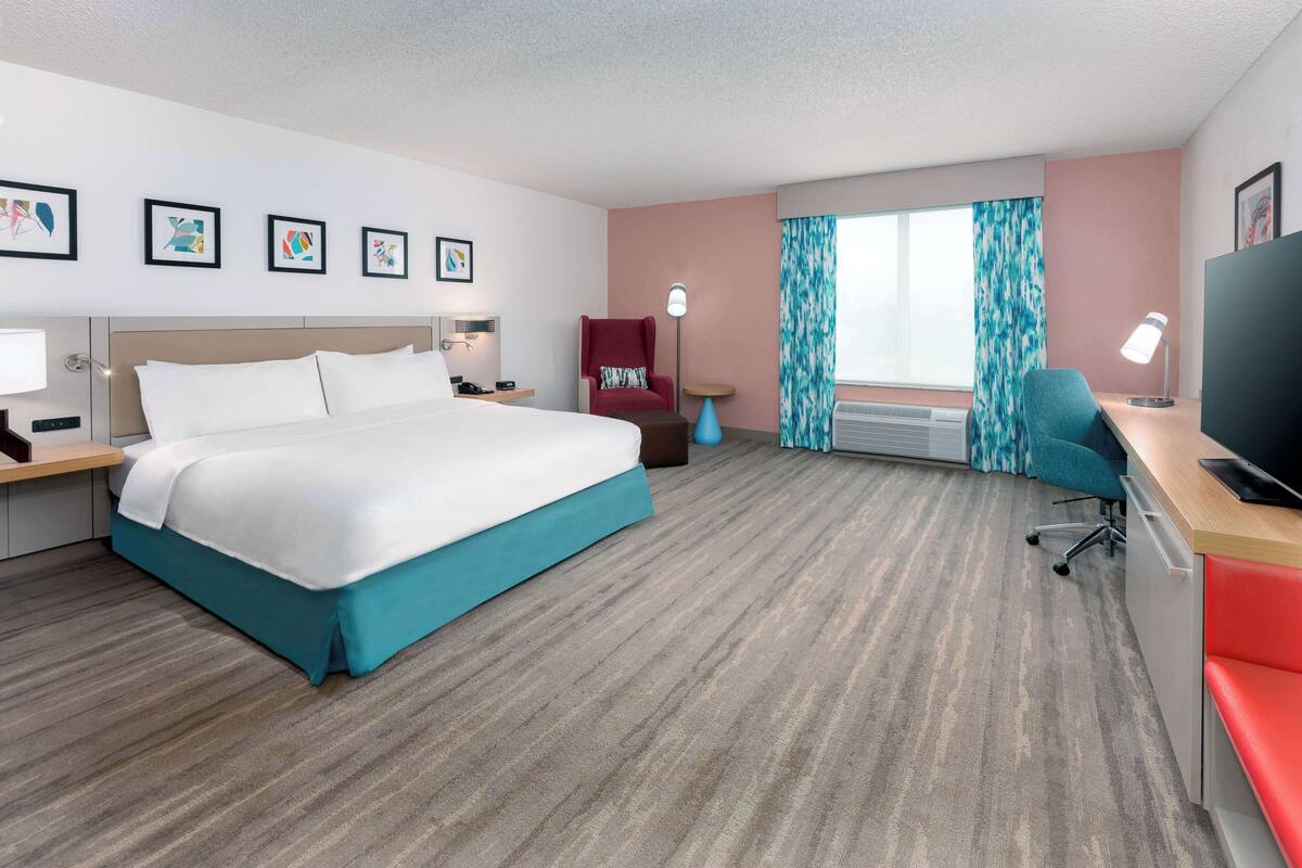 Habitación de hotel con una cama grande, un escritorio con una silla, un televisor y una ventana con cortinas.