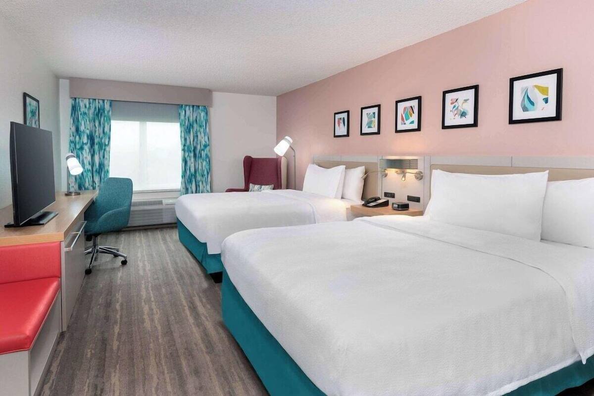 Una habitación de hotel con dos camas, un escritorio, un televisor y una ventana con cortinas.