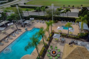 An aerial view of a resort with a swimming pool, lounge chairs, a fire pit, and a well-maintained garden. - Hilton Garden Inn Orlando International Drive North (Orlando)