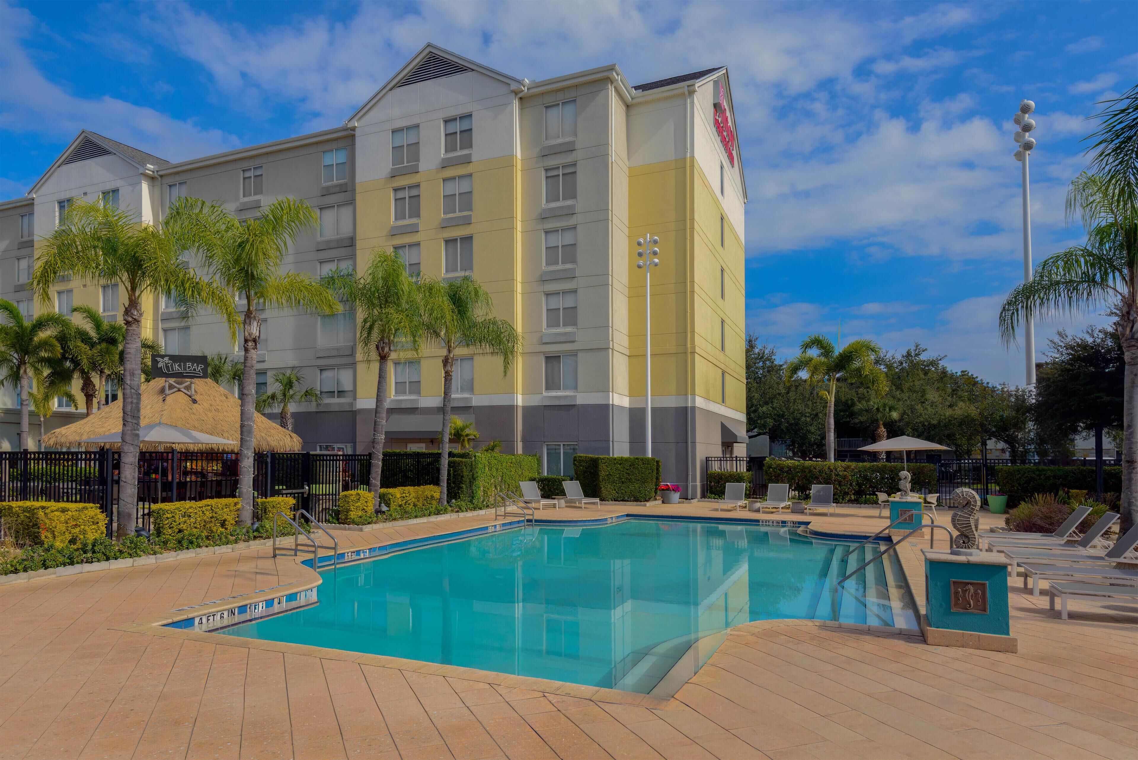 Un hotel con piscina, palmeras y sillones de descanso.