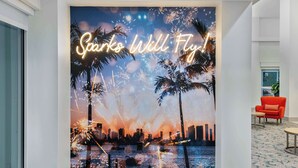 A wall with a neon sign that reads "Sparks Will Fly!" and a cityscape with palm trees.