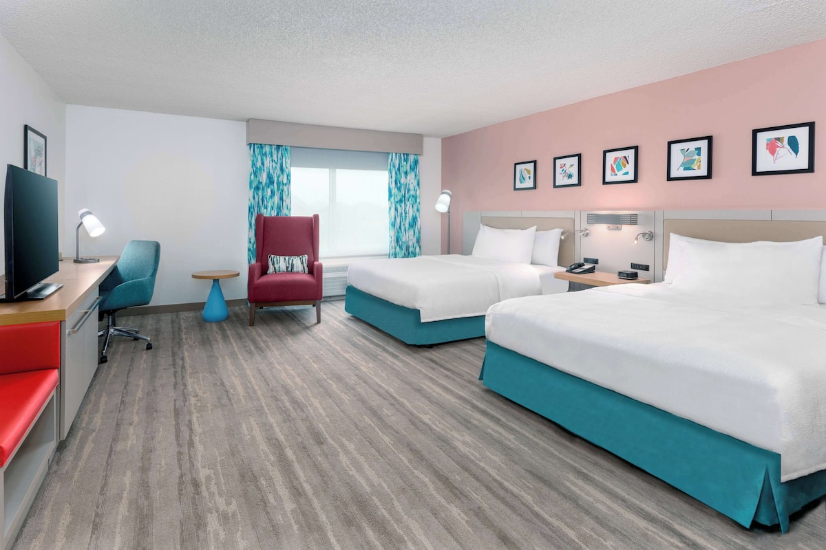 Una habitación de hotel con dos camas, un escritorio con computadora, una silla y un televisor.