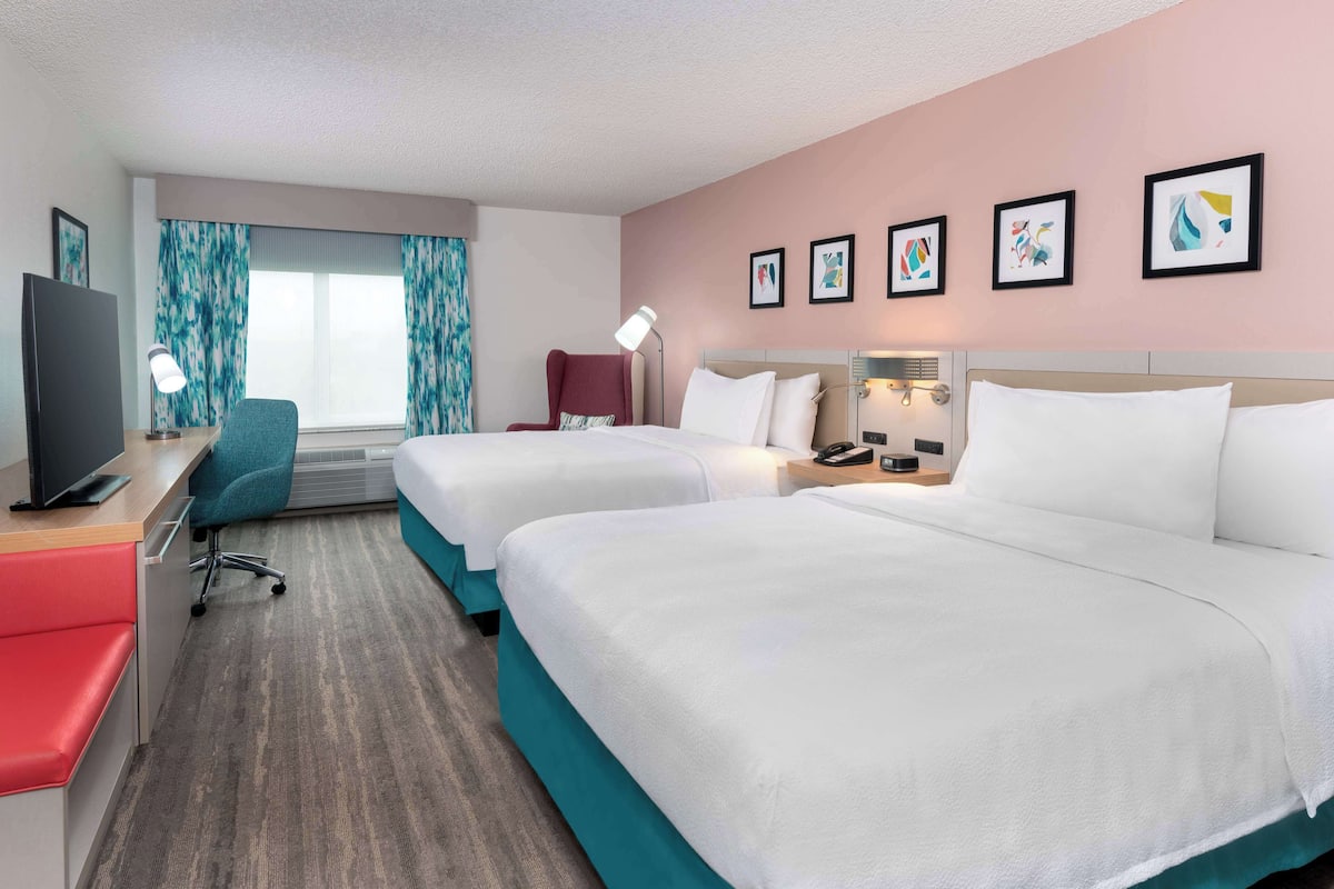 Habitación de hotel con dos camas, un escritorio, un televisor y una silla.
