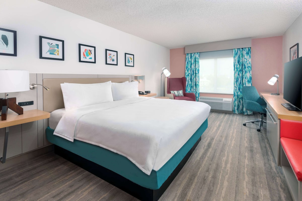 Habitación de hotel con una cama grande, un escritorio con computadora, una silla y un televisor.