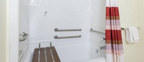 Una bañera con una bandeja de madera, barras de apoyo y una cortina de ducha a rayas.