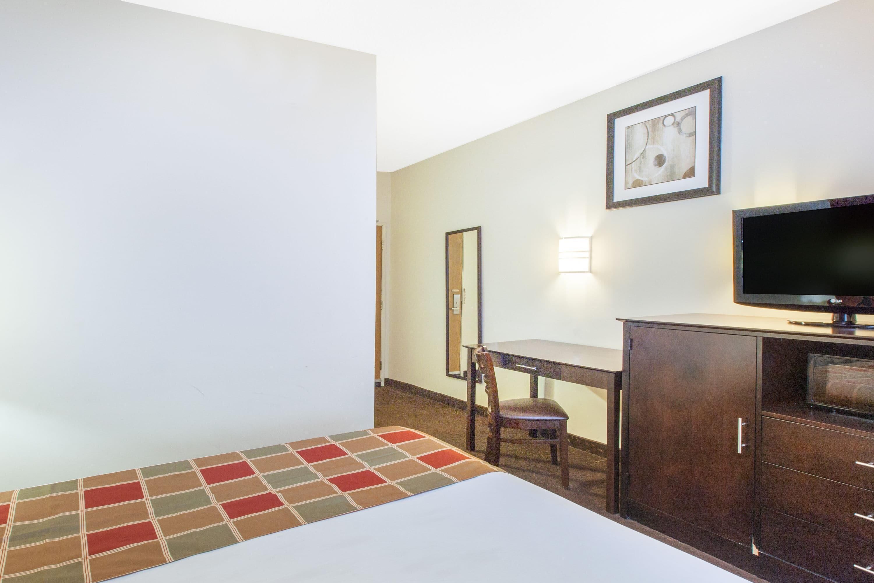 Habitación de hotel con cama, escritorio, silla, televisor y armario.