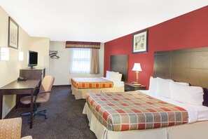 Habitación de hotel con escritorio, dos camas, una silla, televisión y ventana con cortinas.