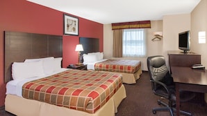 Habitación de hotel con dos camas, un escritorio, una silla, un televisor y una ventana con cortinas.