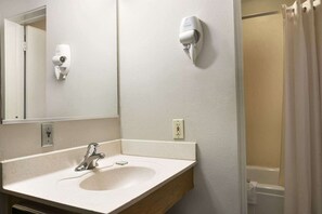 Un baño con lavamanos, espejo, secador de pelo y cortina de ducha.