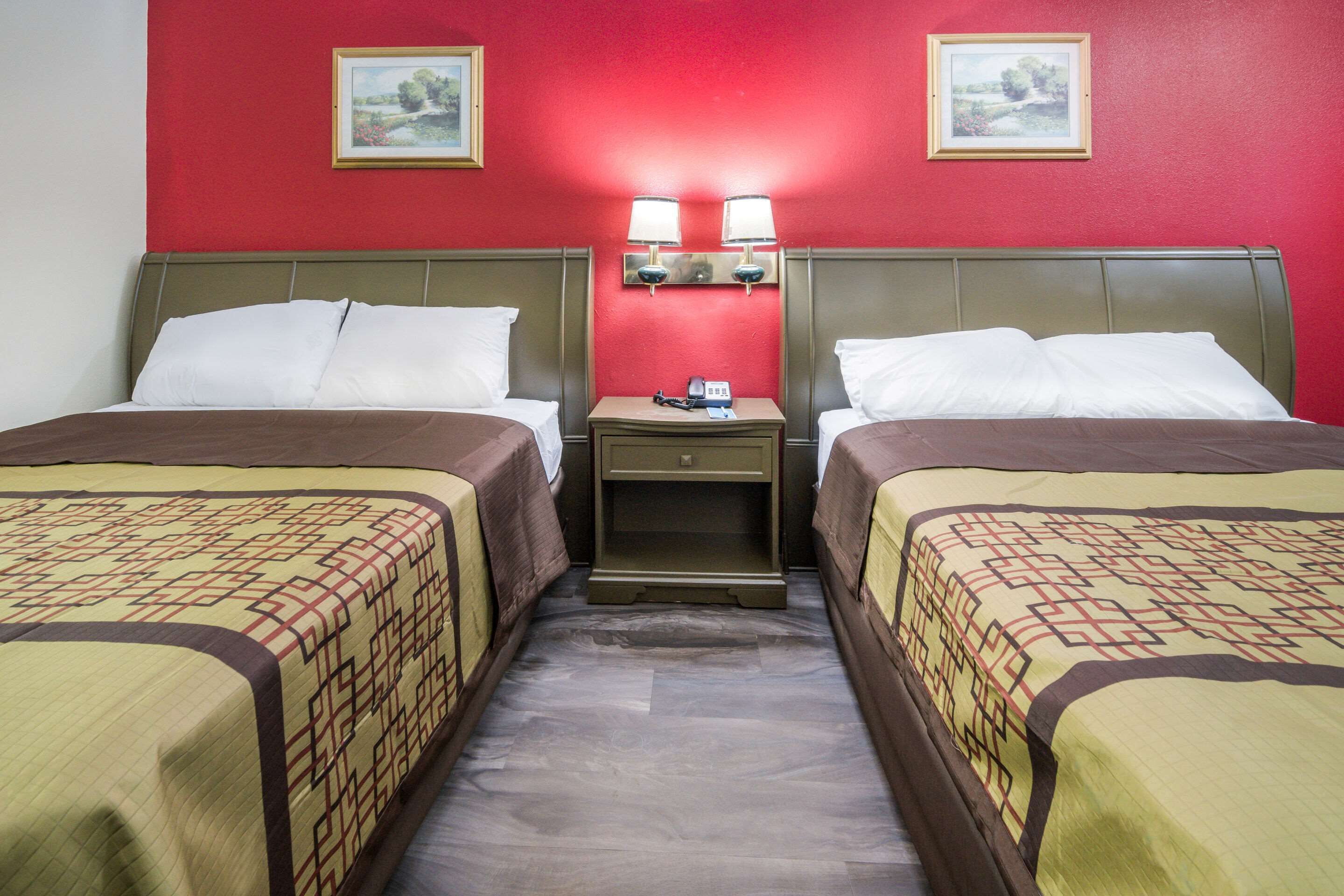 A hotel room with two beds, a nightstand with lamps, and red walls.