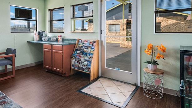 A room with a wooden cabinet, a bulletin board, a door leading outside, and a small table with a potted plant. - Rodeway Inn Ranger I-20 (Ranger)