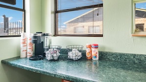 A kitchen counter with a coffee maker, cups, and a coffee container. - Rodeway Inn Ranger I-20 (Ranger)
