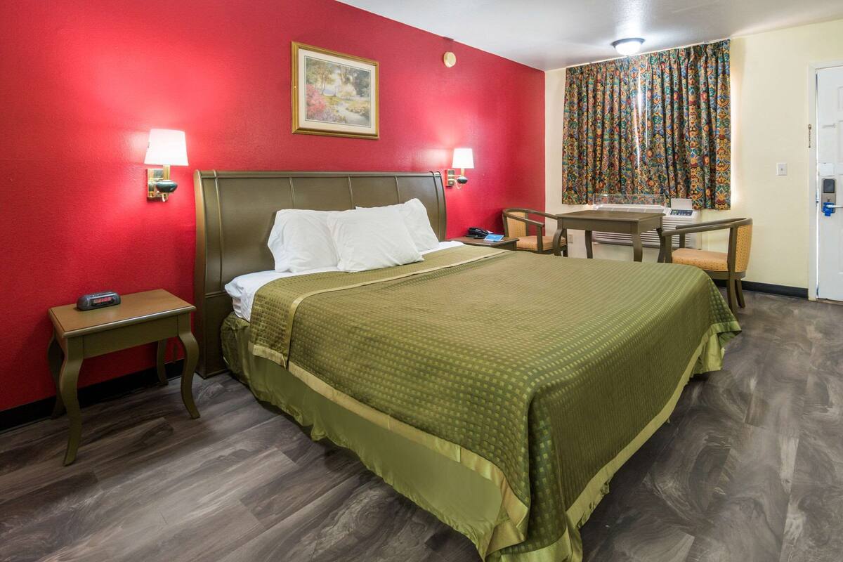 A hotel room with a large bed, two bedside lamps, a desk with a chair, and a window with curtains.