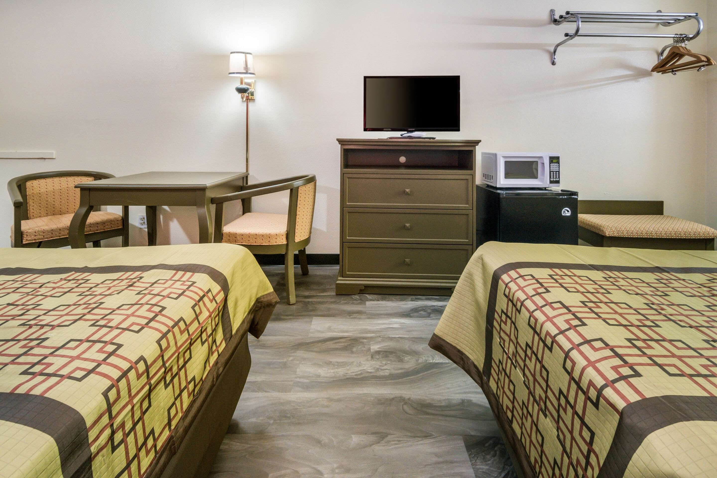 A hotel room with two beds, a desk, a chair, a television, a microwave, and a dresser.