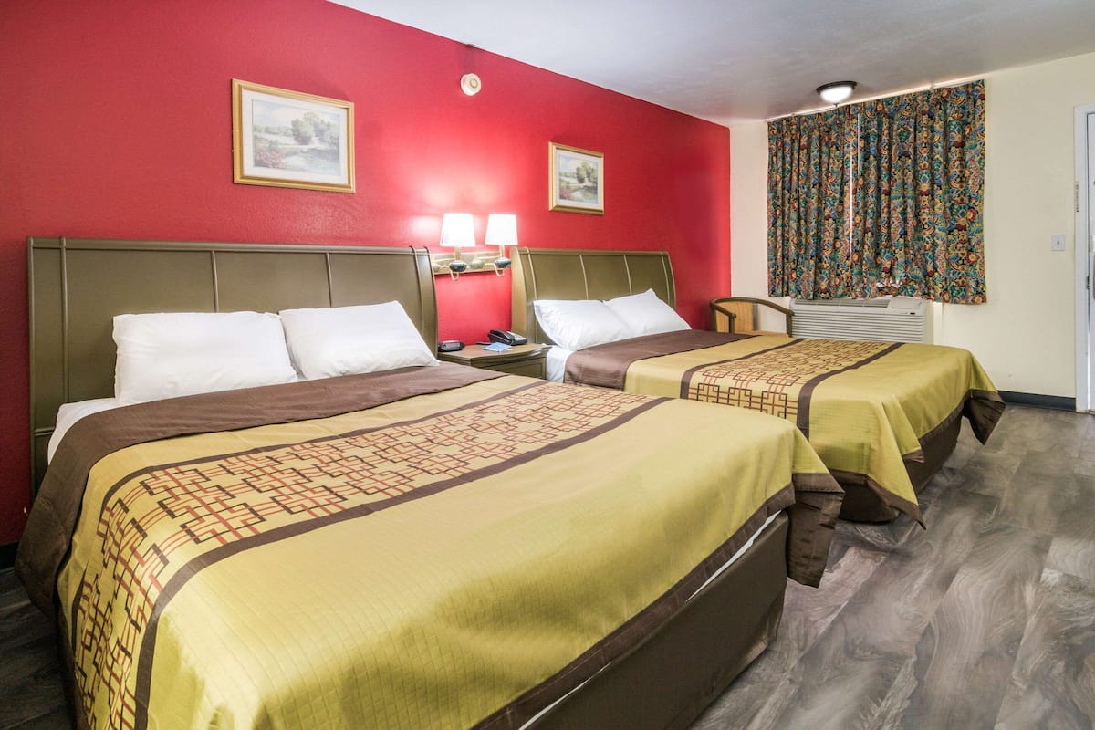 A hotel room with two beds, red walls, and a patterned curtain.