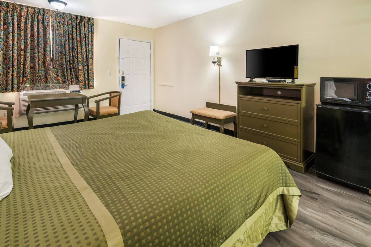 A hotel room with a bed, a desk with a chair, a television, a dresser, and a microwave.