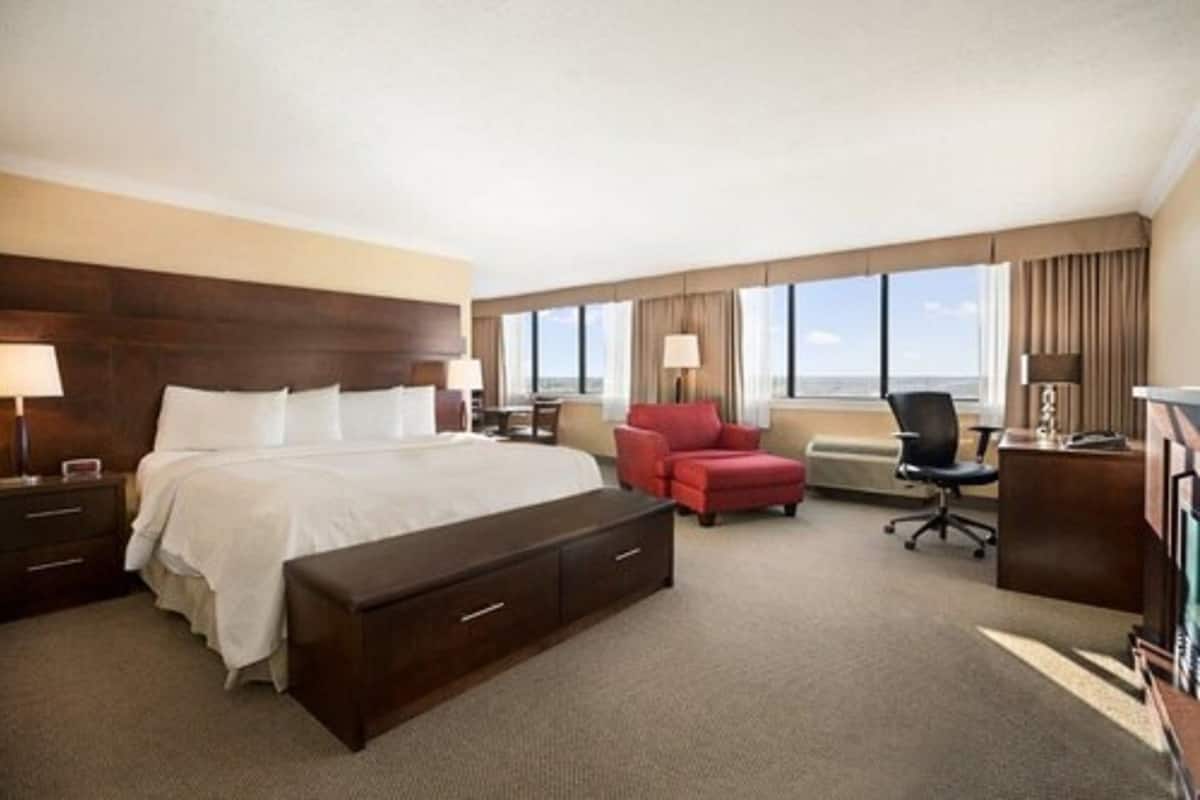 Quarto de hotel com uma cama grande, uma mesa, uma cadeira e vista para o exterior.