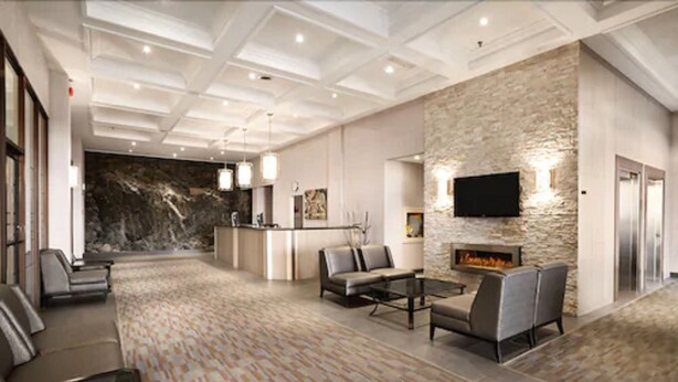 A spacious lobby with a stone wall, a fireplace, and a flat-screen TV mounted on the wall. - The Senator Hotel & Conference Centre Timmins (Timmins)