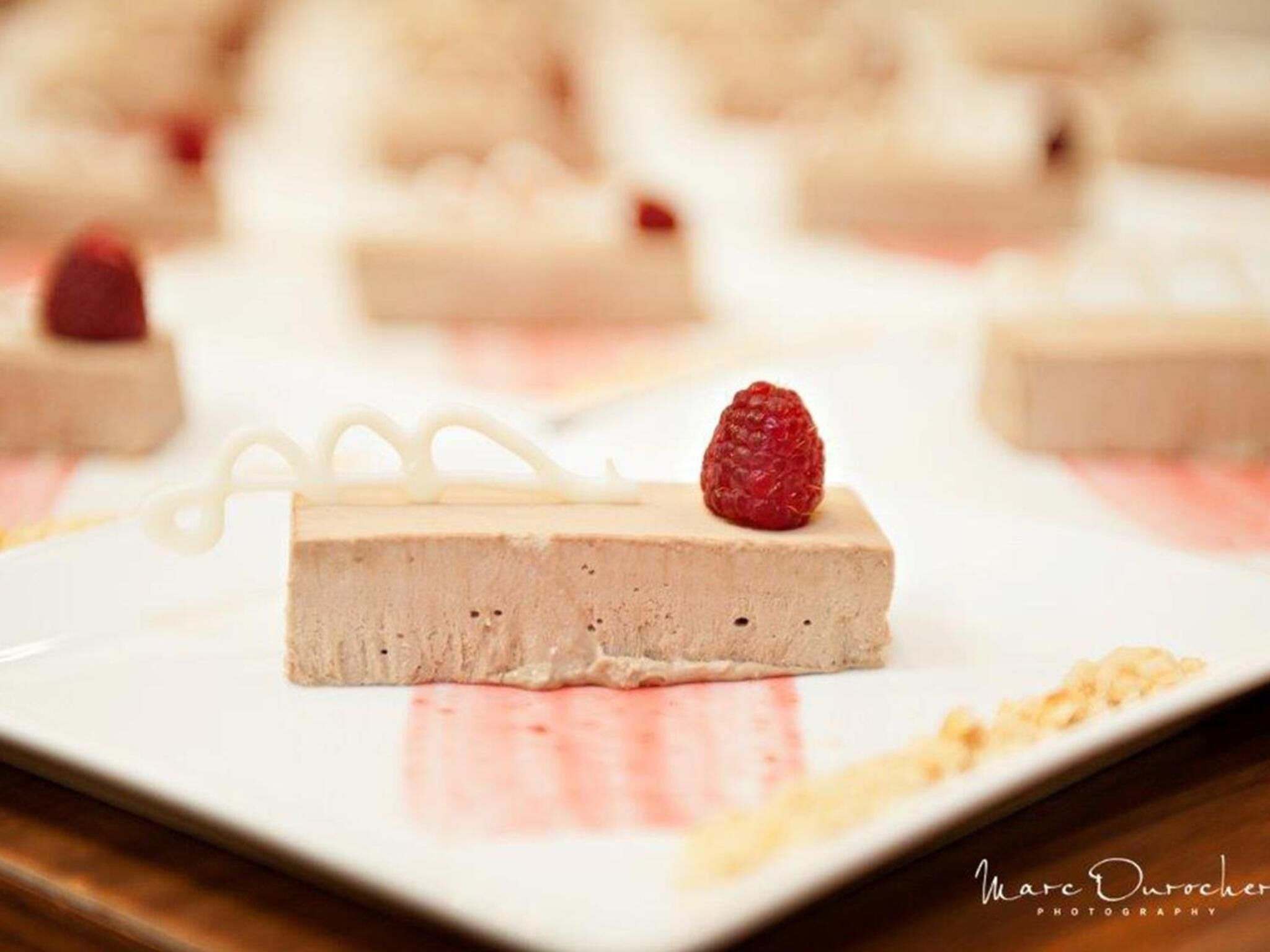 Un postre con una frambuesa encima, sobre un plato blanco.