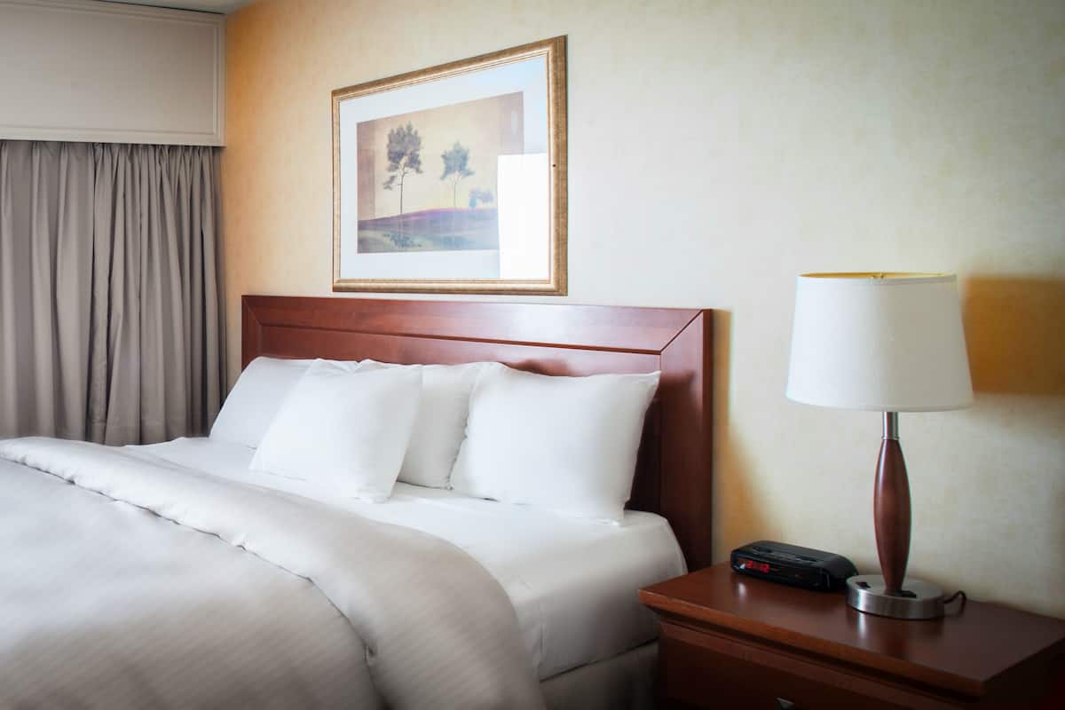 Quarto de hotel com cama bem arrumada, mesa de cabeceira com abajur e quadro na parede.