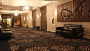 A hotel lobby with a patterned carpet, a sofa, a reception desk, and a wall with a wooden carving. - The Senator Hotel & Conference Centre Timmins (Timmins)