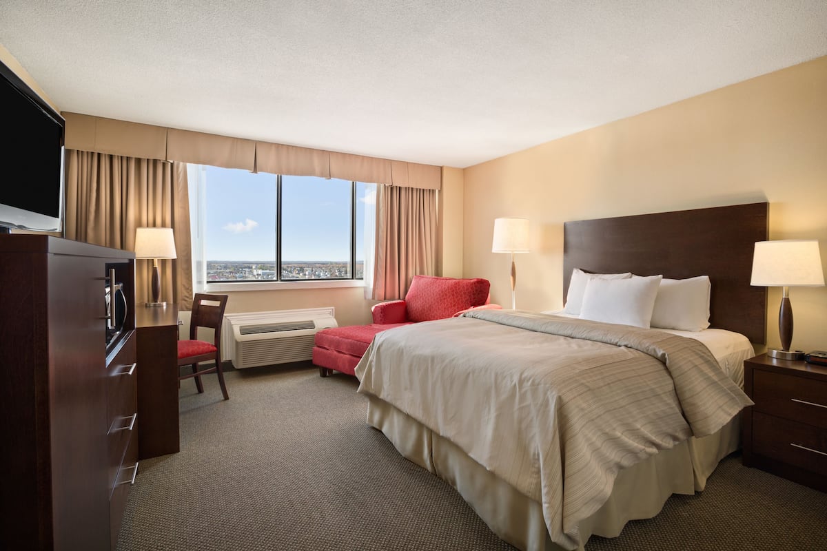 Quarto de hotel com uma cama grande, escrivaninha, cadeira, televisão e janela com vista para a cidade.