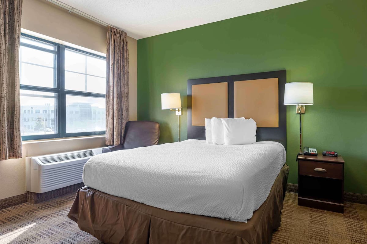 A hotel room with a large bed, two bedside lamps, a chair, a nightstand, and a window with curtains.