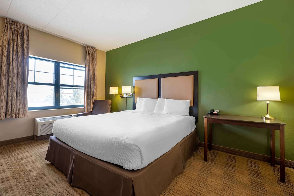 A hotel room with a large bed, a nightstand, a lamp, and a window with curtains.